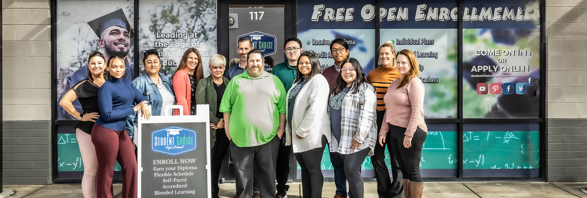 staff in front of school next to enroll now sign