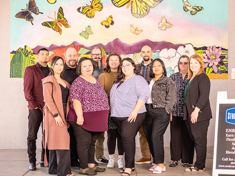 Staff standing in front of wall mural of a field with butterflies ascending from it