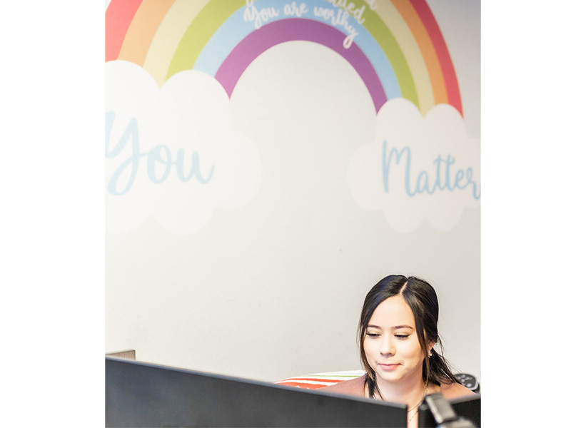 Student sitting under a rainbow with words You Matter painted on wall