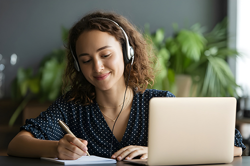 Female high school student wearing headphones and working on a laptop